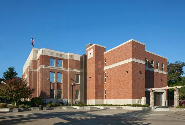 Historic red brick building with clock tower and American flag under clear blue sky.