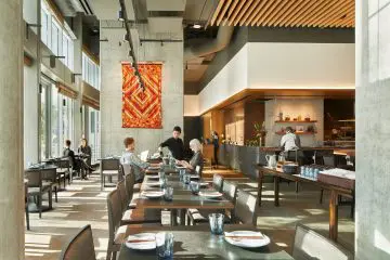 Stylish restaurant interior with modern decor, natural light, and patrons dining. Server attends tables. Contemporary design atmosphere.