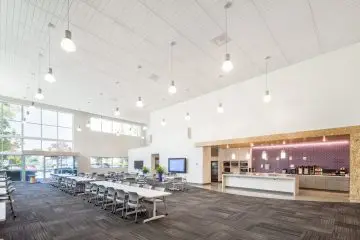 Modern open-plan office space with large windows, ample lighting, seating area, and kitchen amenities. Bright and spacious design.