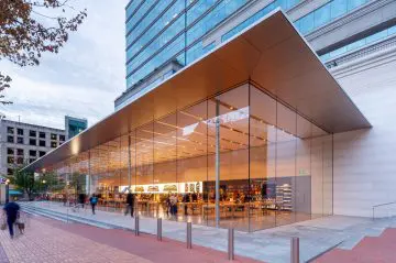 Modern glass-fronted store exterior with pedestrians passing by, featuring a sleek architectural design and city background.