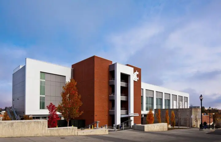 Modern brick and glass building with autumn trees, blue sky backdrop, situated at a university campus.