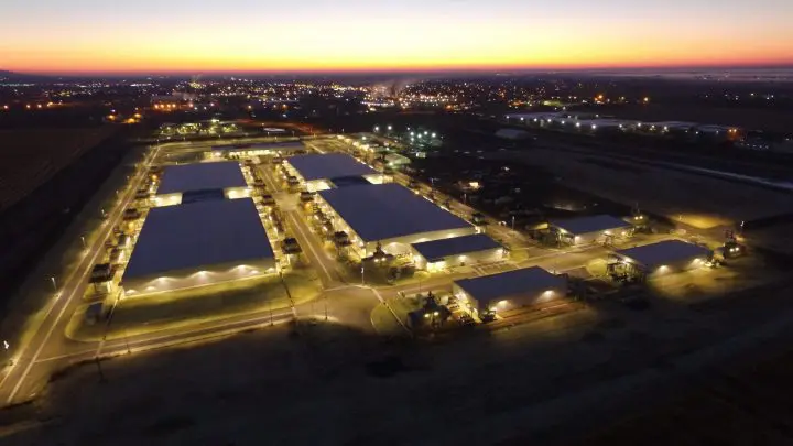 Aerial view of industrial complex at dusk, illuminated buildings and roads under a vibrant sunset sky.