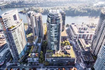 Aerial view of urban high-rise buildings near a river, featuring modern architecture and green rooftops in a bustling cityscape.