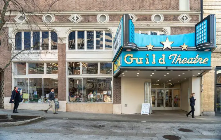 Historic Guild Theatre entrance with vintage marquee, adjacent to a bookstore. People walking by on a city sidewalk.