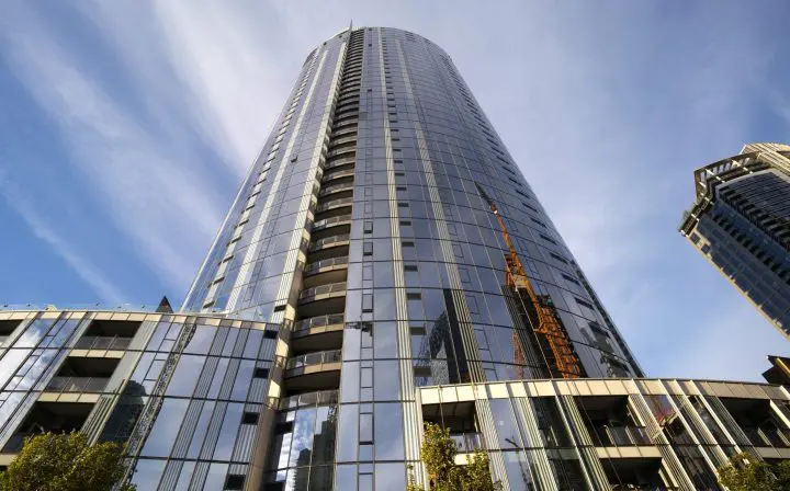 Modern skyscraper with reflective glass facade under a blue sky, angled upwards view. Architectural design and urban development.