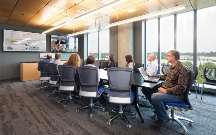Team in modern conference room attending a video call, with collaborative focus on a large screen.
