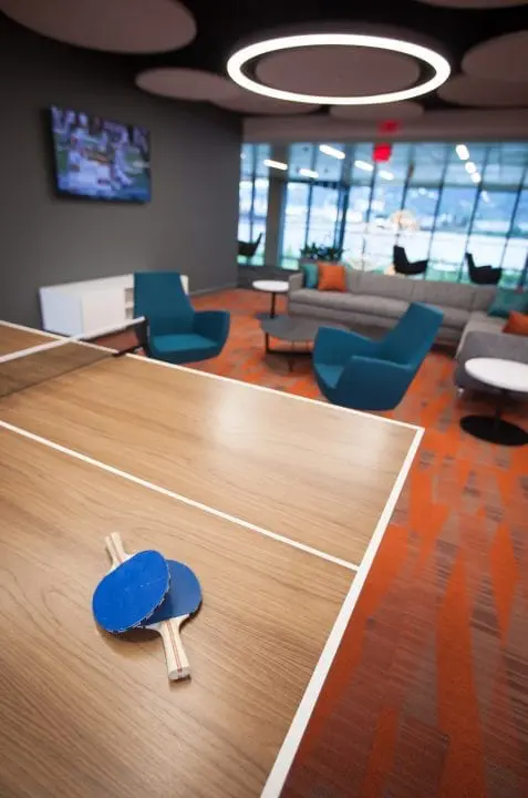 Modern lounge with ping pong table and paddles, vibrant seating, and large windows. Cozy ambiance for relaxation or play.