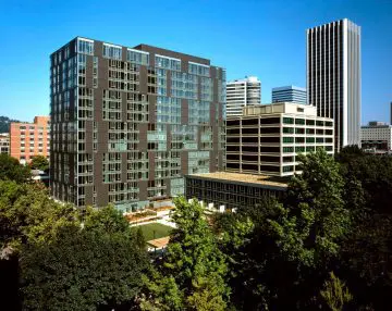 Modern urban buildings with lush green trees beneath a clear blue sky, showcasing city architecture and nature harmony.