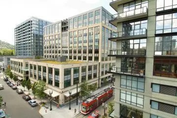 Modern urban buildings with a red streetcar passing through a bustling city street, surrounded by glass architecture.
