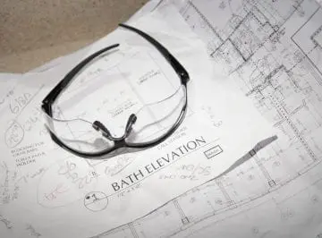 Safety glasses on architectural plans with handwritten notes for bath elevation.