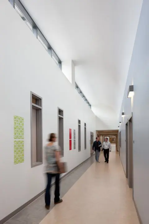 Modern corridor with high ceilings, featuring art on walls. People walk down the hallway, creating a sense of motion and activity.