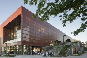 Modern research center exterior with glass and metal facade, people gathering outside under a clear sky with trees in the foreground.