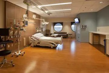 Modern hospital room with medical equipment, bed, and seating area, designed for comfort and care.