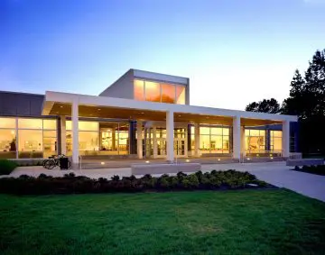 Modern building exterior at twilight, featuring large windows and a welcoming entrance with surrounding greenery.