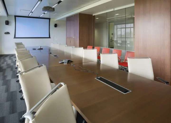 Modern conference room with large table, white chairs, projector screen, and glass wall. Ideal for meetings and presentations.