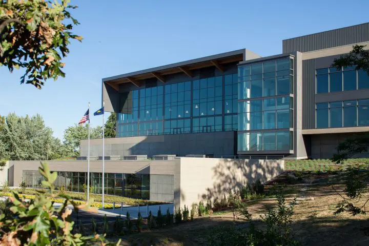 Modern glass building exterior with flags and landscaped greenery, under clear blue sky. Sustainable architecture and design.