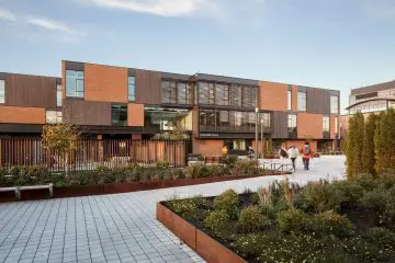 Modern university building with landscaped courtyard and people walking. Sunny day, clear skies.