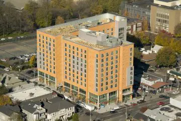 Aerial view of an urban mid-rise building with a green rooftop, surrounded by streets and trees.