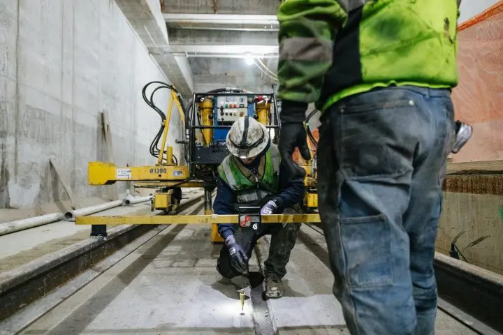 Construction workers measuring rail alignment in an underground tunnel.