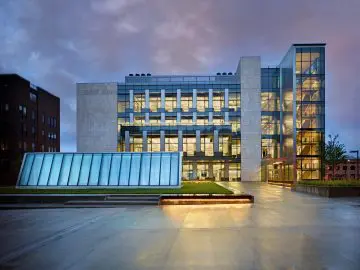 Modern glass and stone building at dusk with colorful sky, featuring lit windows and architectural details for a sleek design.