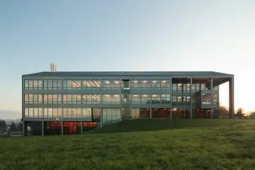 Modern glass office building at sunrise, surrounded by a green lawn. Sustainable architecture and innovative design.