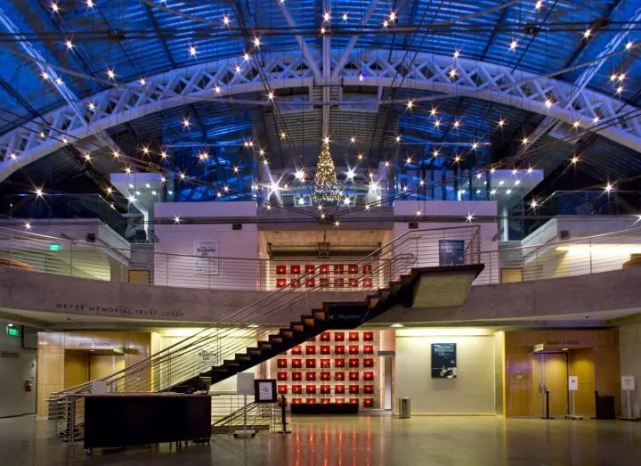 Modern lobby with illuminated staircase and a high ceiling. Decorative lights and a festive atmosphere create a welcoming space.