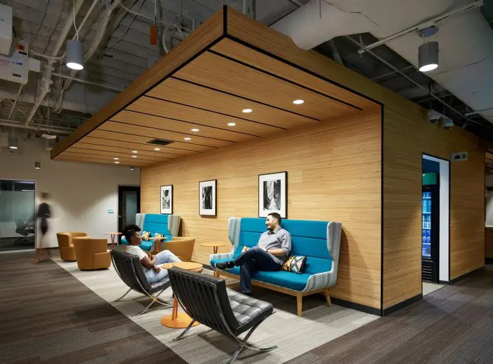 Modern office lounge with a casual meeting area, featuring comfortable seating, wooden accents, and monochrome artwork on the walls.