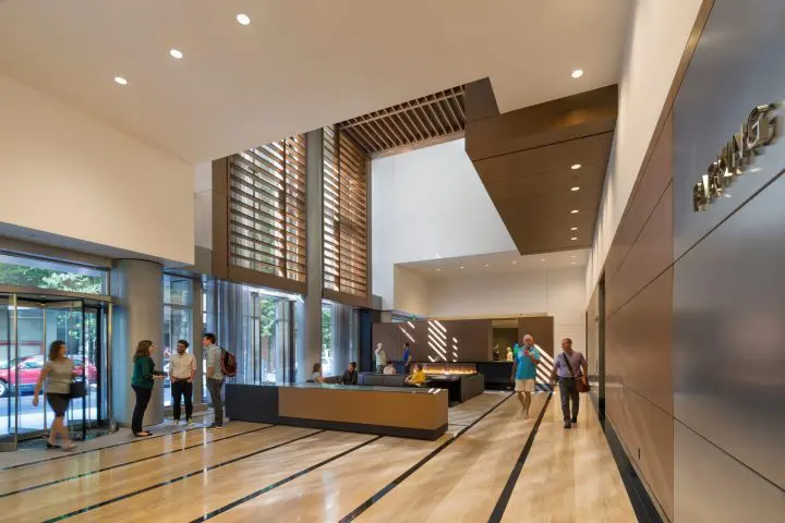 Modern office lobby with people interacting. Bright, spacious area with seating, reception desk, and large windows for natural light.