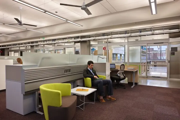 Modern office space with glass walls, green chairs, and working individuals. Quiet, professional atmosphere.