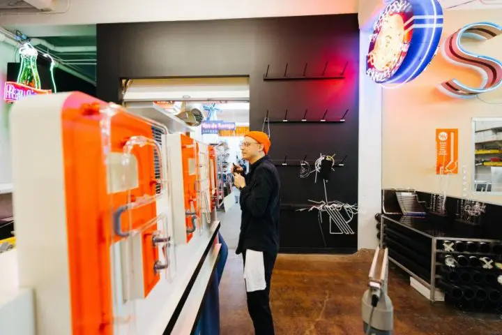 Person in orange hat explores neon-lit store with signage and eclectic decor.