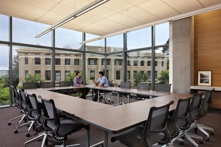 Two people meeting in a modern conference room with large windows and a view of a historic building outside.