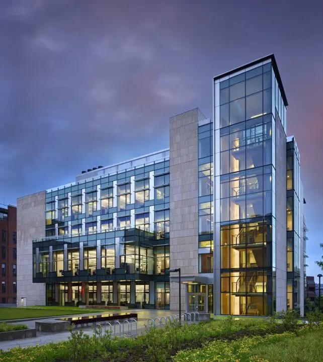 Modern glass and stone building with lit interiors at twilight, set against a cloudy sky. Urban architecture and design concept.