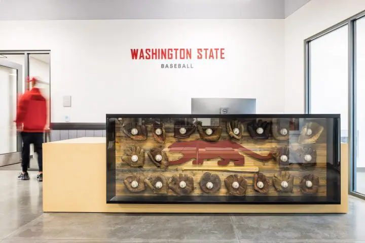 Washington State baseball lobby with glove display and red logo. Person in red hoodie walking through entrance. Modern, sleek design.
