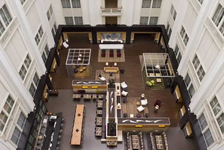 Spacious hotel atrium with modern seating areas, tables, and wooden flooring, viewed from above.