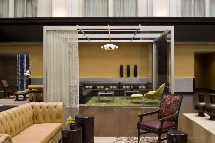 Modern hotel lobby with elegant seating, glass partition, and decorative accents, featuring brown and green tones for a cozy ambiance.