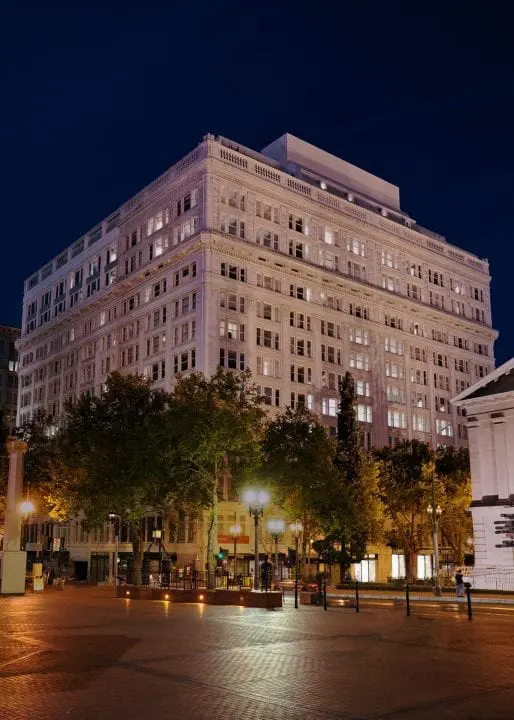 Illuminated historic building at night with trees in the foreground, showcasing urban architecture and city lights.