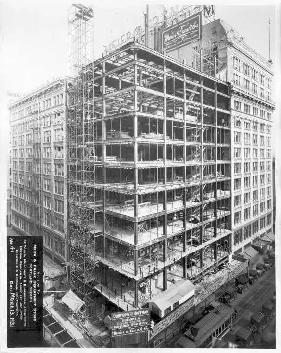 Historic building under construction in urban setting, showcasing steel framework and bustling street below.