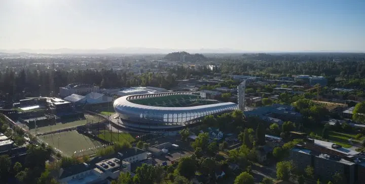 Aerial view of a modern sports stadium surrounded by cityscape and greenery under a clear blue sky.