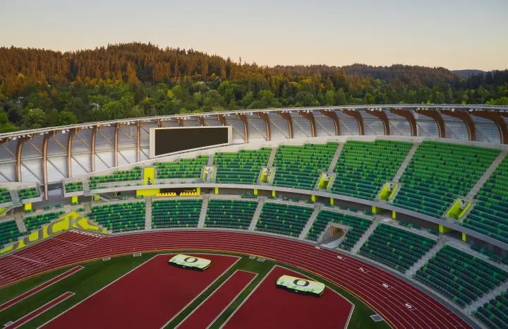 Stadium with green seats and a red track, surrounded by lush trees under a clear sky, offering a serene sporting venue ambiance.