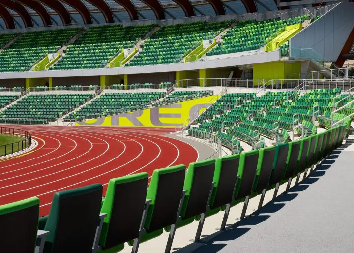 Empty athletic stadium with red running track and green seating, ready for events.