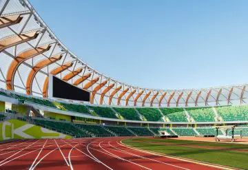 Modern outdoor stadium with green seating and red running track under a clear blue sky.