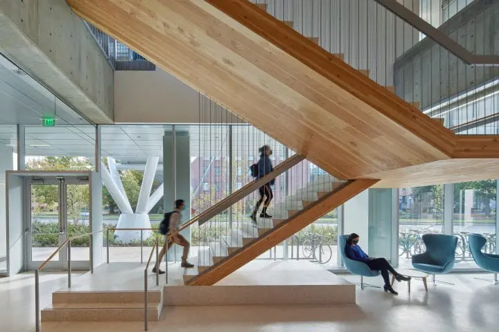 Modern building interior with people on stairs and seating. Open space, wood accents, and natural light enhance the contemporary design.