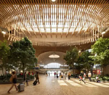 Spacious train station interior with wooden ceiling design, natural light, and travelers moving around, creating an open and modern atmosphere.