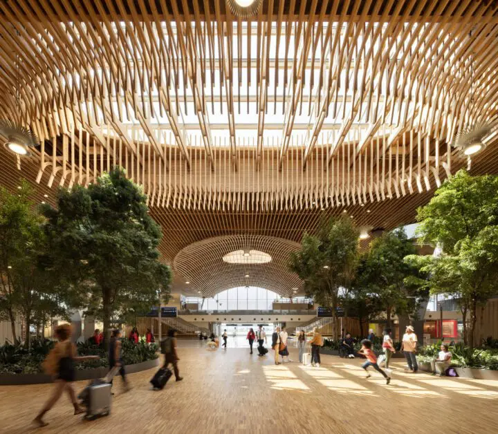 Spacious train station interior with wooden ceiling design, natural light, and travelers moving around, creating an open and modern atmosphere.