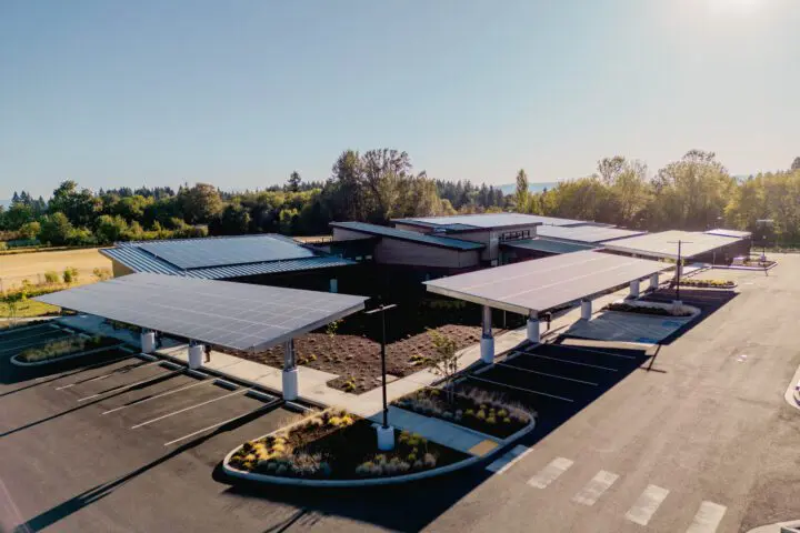 Aerial view of modern building with solar panel carports in a lush park setting, promoting sustainable energy solutions.