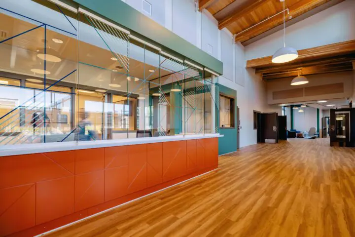Modern office lobby with wooden floors, high ceilings, and colorful reception desk. Spacious and inviting design.
