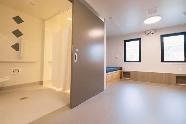 Modern hospital room with a sliding door, accessible bathroom, and bed by two large windows. Bright, clean, and minimalistic design.