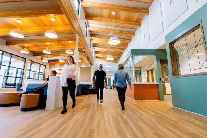 Modern office space with people walking on wood flooring under stylish lighting and high ceilings.