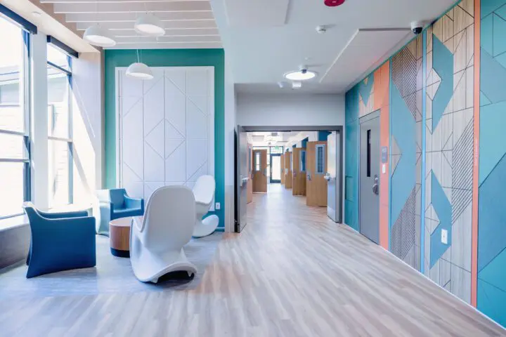 Modern hallway with geometric wall designs, natural lighting, and stylish seating area. Bright and inviting interior space.