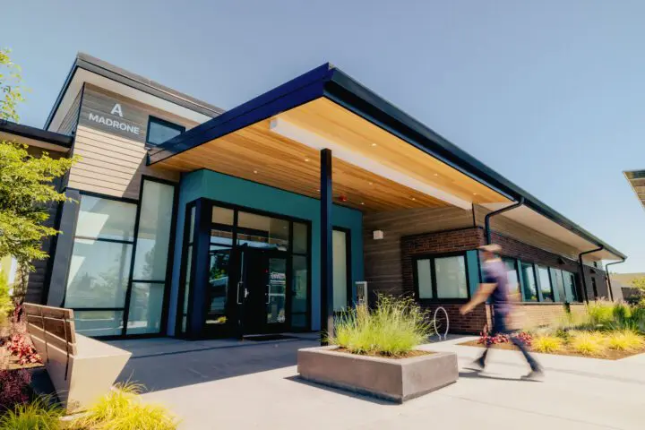 Modern commercial building with sleek architecture, featuring wood accents and large windows. Person walking past entrance.